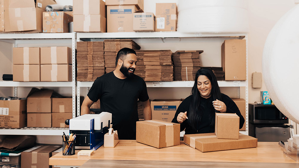 two people standing in front of a packing table surrounded by boxes